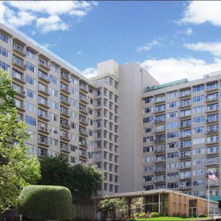A tall apartment building with numerous windows, set against a bright blue sky and surrounded by greenery.