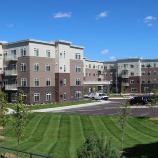 A modern apartment complex with well-maintained landscaping under a clear blue sky.