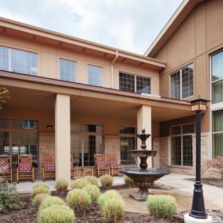 A modern building exterior with a patio area featuring a fountain and landscaping.