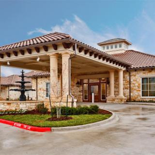 The entrance of a modern building featuring elegant architecture and well-maintained landscaping.