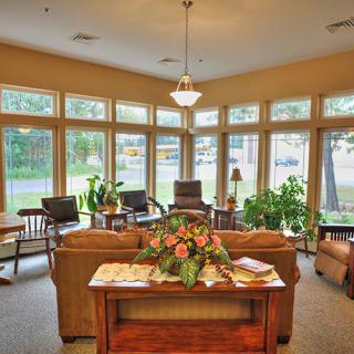 A cozy living room with large windows, featuring comfortable seating and indoor plants.