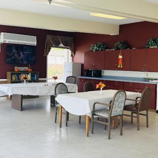 A spacious dining area with tables and chairs, featuring a kitchenette against red walls.