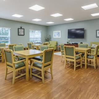 A spacious meeting room with multiple tables and chairs, featuring a television on the wall.