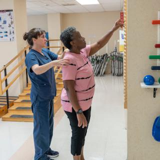 A physical therapist assists a patient in reaching for an object as part of a rehabilitation exercise.