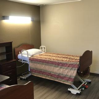 A clean and organized patient room in a healthcare facility, featuring a hospital bed and bedside furniture.