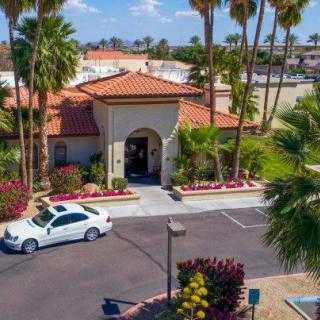 A scenic view of a tropical building with a car parked in the driveway, surrounded by palm trees.