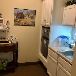 A small kitchen area with cabinets, a sink, microwave, and a painting on the wall.