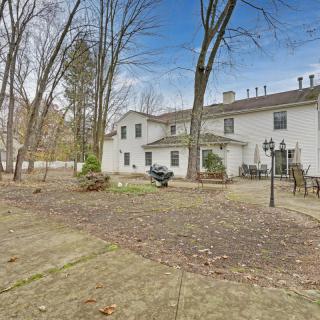 A spacious backyard with a large white house, patio area, and surrounding trees.