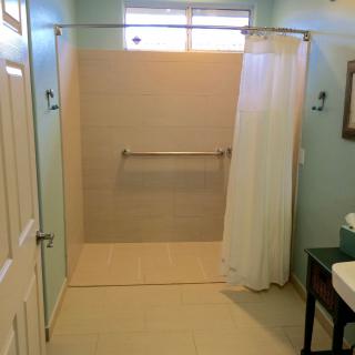 A minimalist bathroom features a spacious shower with a curtain, a towel rack, and a modern sink.