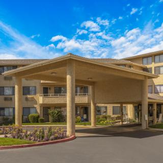 The exterior view of a hotel entrance with a covered driveway and landscaped surroundings on a clear day.