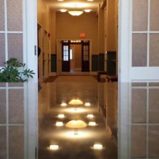 A polished hallway with reflections of ceiling lights on the shiny floor, leading to a set of double doors.