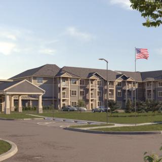 A large residential apartment complex with an American flag flying in front, surrounded by a parking lot.
