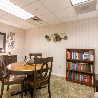 A cozy meeting room with a round table, chairs, and a bookshelf filled with books.