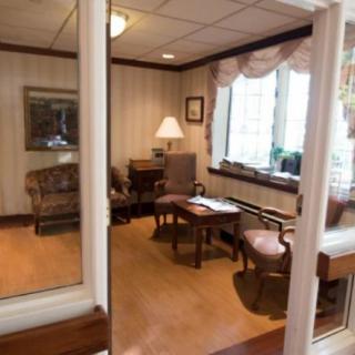 A cozy office space with a desk, chairs, and a lamp near a large window.