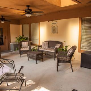 A cozy patio with comfortable rattan seating, ceiling fans, and lush potted plants.