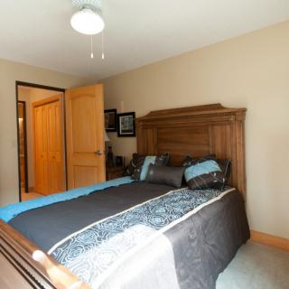 A cozy bedroom featuring a wooden bed frame with blue and gray bedding, enhanced by warm lighting and simple decor.