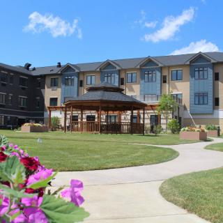 A peaceful garden with a gazebo in front of a large building under a clear blue sky.