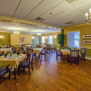 A well-lit dining room with neatly arranged tables and chairs on a wooden floor.