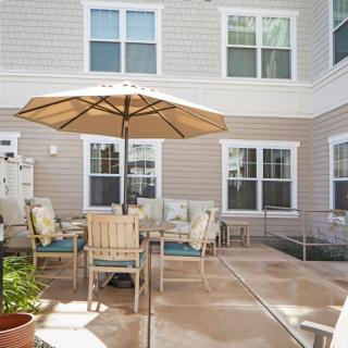 A cozy outdoor patio area featuring a table with chairs and an umbrella, set against the backdrop of a building exterior with multiple windows.