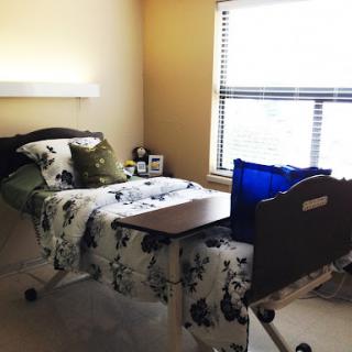 A cozy bedroom featuring a hospital bed, decorative bedding, and natural light from the window.