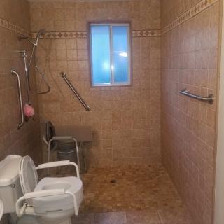 An accessible bathroom with a tiled shower area, featuring grab bars and a shower chair for safety.