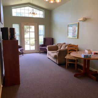 A spacious living room with a sofa, table, and chairs, featuring large windows that allow natural light to fill the space.