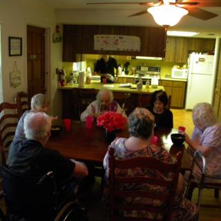 A group of seniors gathered around a dining table in a homey kitchen setting.