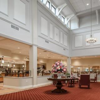 A spacious lobby with elegant architectural details, featuring a central floral arrangement and chandeliers.