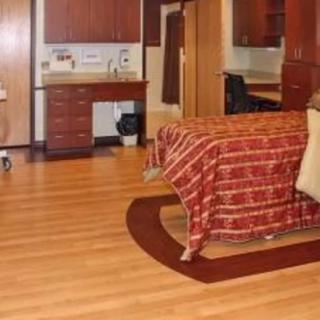 A hospital room featuring a patient bed and medical equipment with wooden flooring.