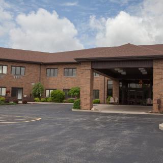 A two-story brick hotel with a covered entrance and a surrounding parking area under a cloudy sky.