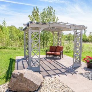 A sunny outdoor garden featuring a pergola with a bench underneath.