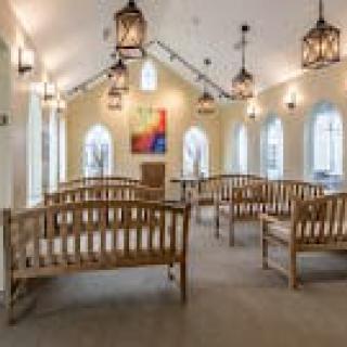 A serene chapel interior with wooden benches and hanging lanterns.
