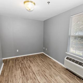 An empty room with gray walls, wood flooring, a ceiling light, a window, and an air conditioning unit.