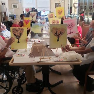 A group of elderly individuals enjoys a painting session, showcasing their artwork and engaging in creative expression.