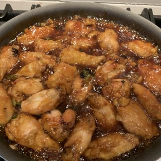 Chicken wings simmering in a flavorful sauce on the stove.