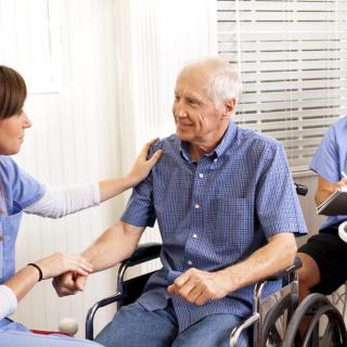 A caregiver providing support to an elderly man in a wheelchair.