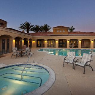 A serene evening view of a luxurious outdoor swimming pool and hot tub area, surrounded by palm trees.