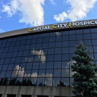 A modern building with a glass facade reflecting clouds, identified as Capital City Hospice.