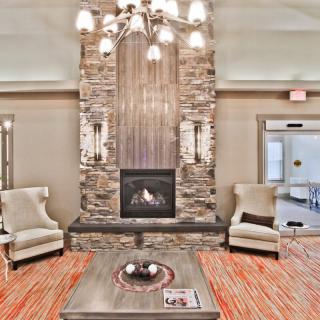 A cozy living room featuring a stone fireplace, armchairs, and a chandelier.