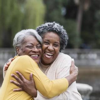 Two senior women embracing and smiling outdoors, enjoying their friendship.