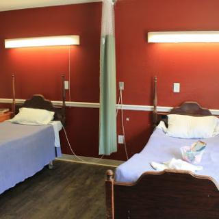 A hospital room featuring two beds with a warm red wall backdrop.