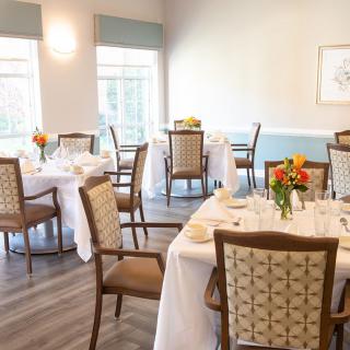 A bright and elegant dining area with tables set for guests, decorated with flowers and white tablecloths.