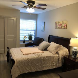 A cozy bedroom with a neatly made bed, a ceiling fan, and natural light coming through the window.
