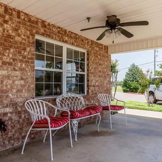 A cozy porch with brick walls featuring white metal chairs with red cushions and an overhead ceiling fan.