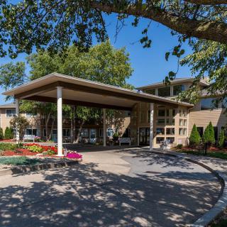 A covered entrance to a building surrounded by trees and colorful flowers on a sunny day.