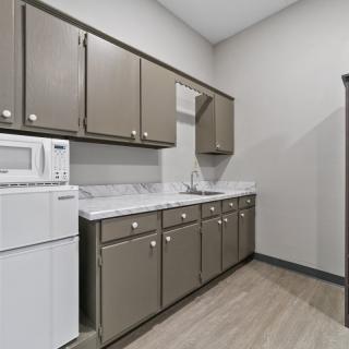 A modern kitchen with gray cabinets and a white countertop, featuring a microwave and sink.
