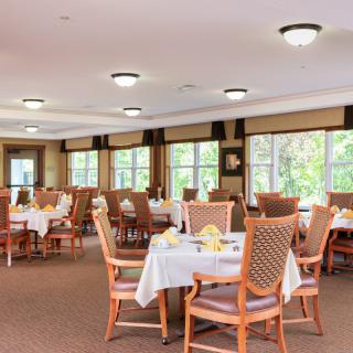 A spacious dining area with neatly arranged tables and chairs, featuring large windows and warm lighting.