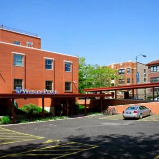 A brick hospital building with a parking lot and car on a clear day.