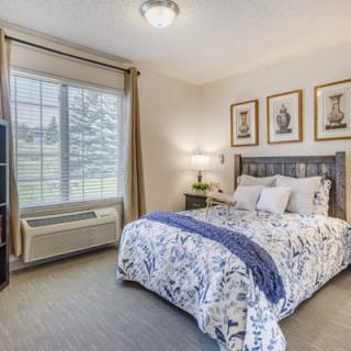 A cozy bedroom with a stylish bedspread, elegant artwork, and natural light coming through the window.