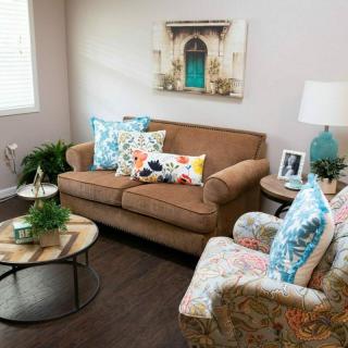 A cozy living room with a brown sofa, floral cushions, and a decorative armchair beside a round coffee table.